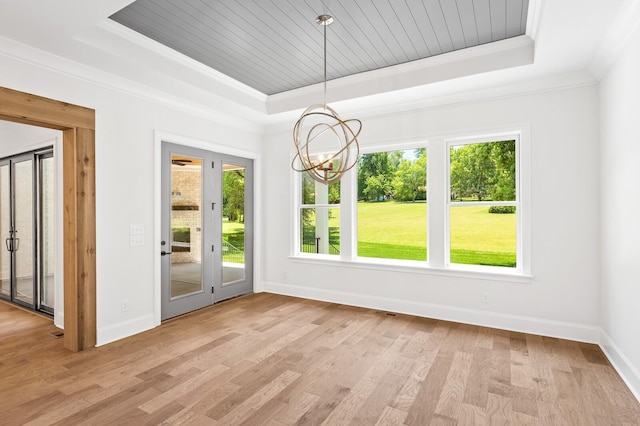 unfurnished dining area featuring light wood-style flooring, a tray ceiling, baseboards, and ornamental molding