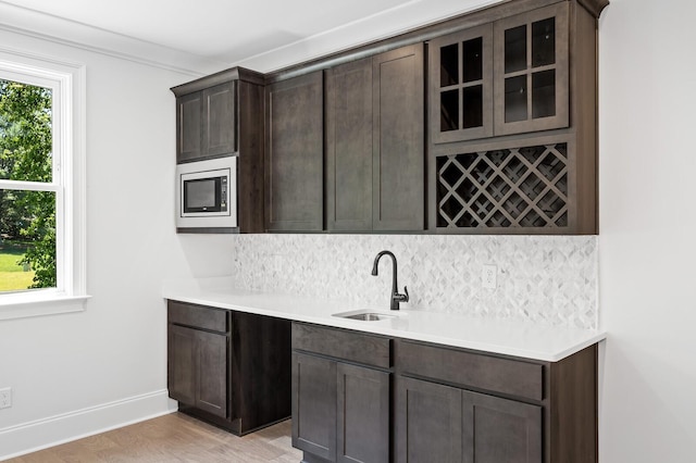 kitchen with tasteful backsplash, stainless steel microwave, a sink, and dark brown cabinetry