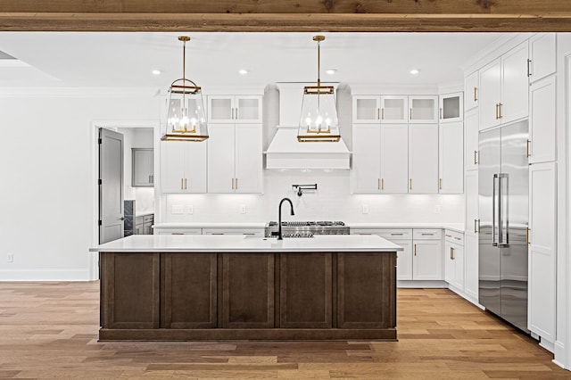 kitchen with light wood-type flooring, light countertops, stainless steel built in fridge, and custom range hood