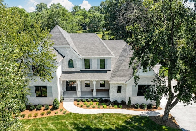 french country home featuring roof with shingles, a porch, and a front lawn