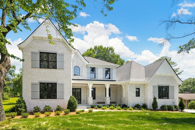 view of front of house with covered porch, brick siding, and a front yard