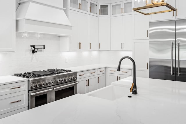 kitchen with a sink, premium range hood, white cabinetry, and premium appliances