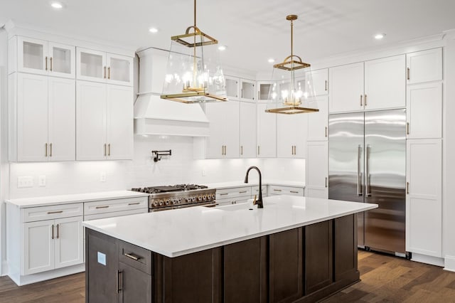 kitchen with high end appliances, a kitchen island with sink, light countertops, white cabinetry, and a sink