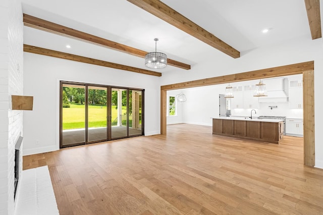 unfurnished living room with light wood finished floors, baseboards, a notable chandelier, and beamed ceiling