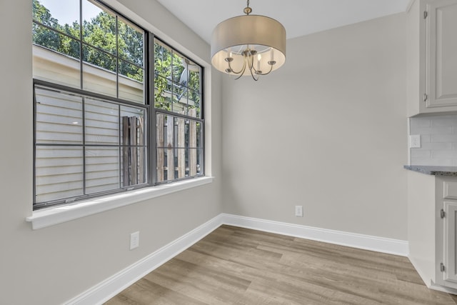 unfurnished dining area with baseboards, light wood-type flooring, and an inviting chandelier