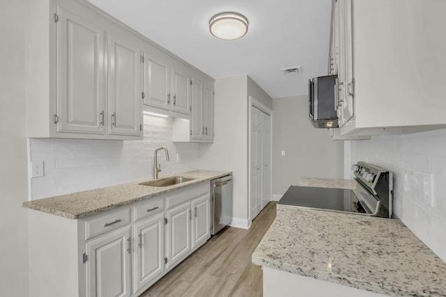 kitchen featuring white cabinets, light wood-style flooring, stainless steel appliances, and a sink