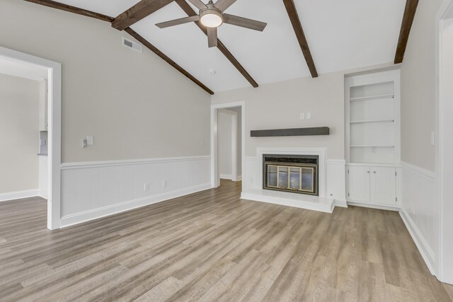 unfurnished living room with built in shelves, visible vents, lofted ceiling with beams, a glass covered fireplace, and wood finished floors