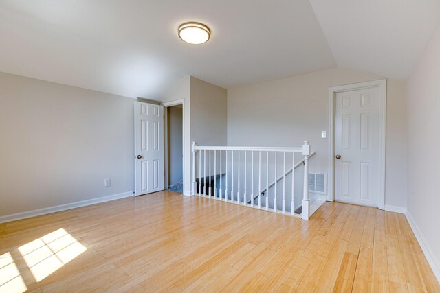 empty room with vaulted ceiling, light wood-type flooring, visible vents, and baseboards