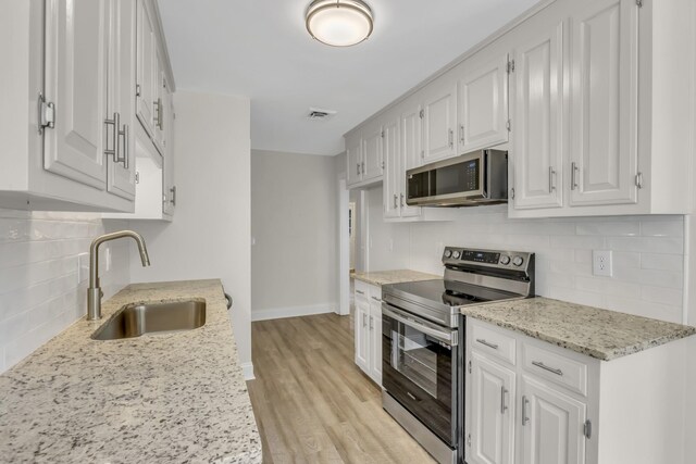 kitchen with light wood-style flooring, stainless steel appliances, a sink, visible vents, and white cabinets