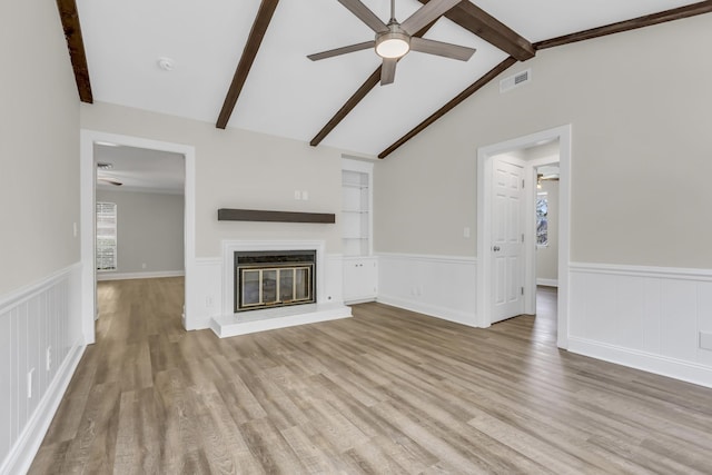 unfurnished living room with ceiling fan, lofted ceiling with beams, wood finished floors, visible vents, and a glass covered fireplace