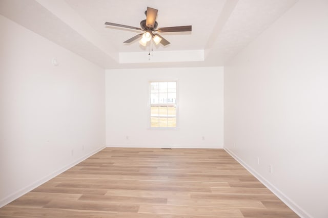 spare room with light wood-type flooring, ceiling fan, a tray ceiling, and baseboards