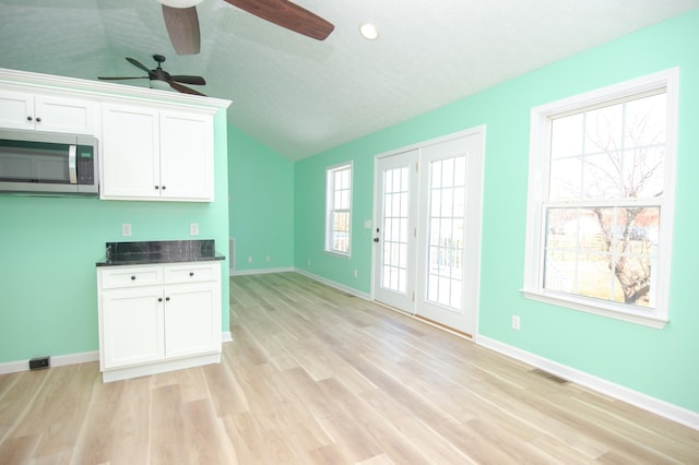 kitchen with visible vents, baseboards, white cabinetry, light wood-type flooring, and stainless steel microwave