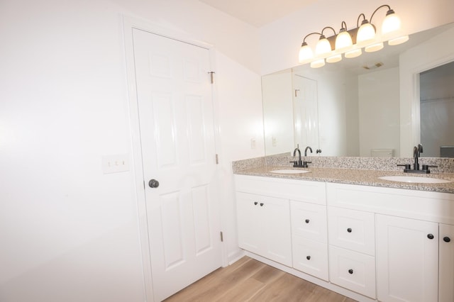 full bath with double vanity, visible vents, a sink, and wood finished floors