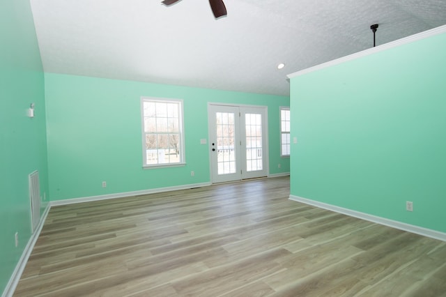 spare room with baseboards, a ceiling fan, light wood-style flooring, vaulted ceiling, and a textured ceiling