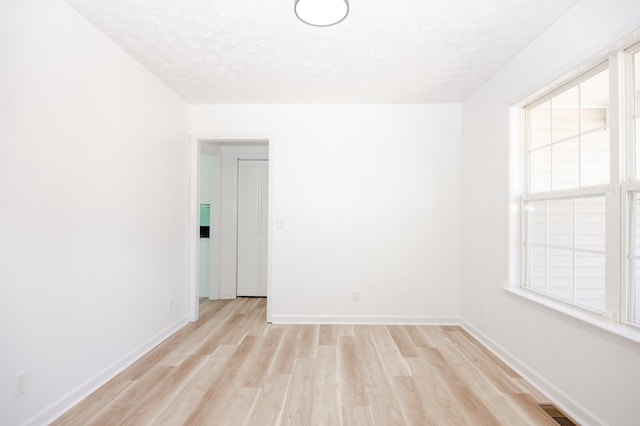 empty room featuring visible vents, light wood-style flooring, a wealth of natural light, and baseboards