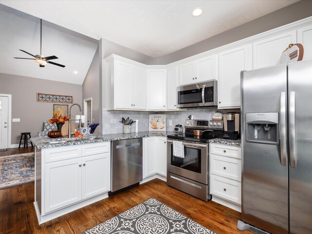 kitchen featuring white cabinets, appliances with stainless steel finishes, a peninsula, light stone countertops, and a sink