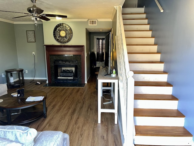 stairs with a fireplace, wood finished floors, a ceiling fan, visible vents, and crown molding