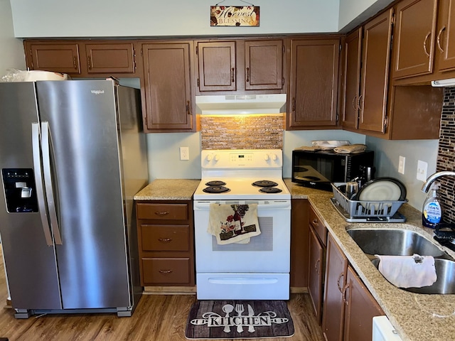 kitchen with white electric stove, black microwave, under cabinet range hood, a sink, and stainless steel fridge