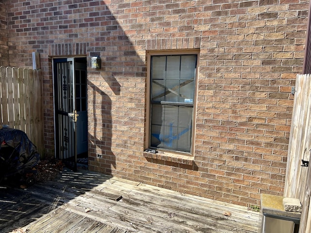 view of exterior entry with fence and brick siding