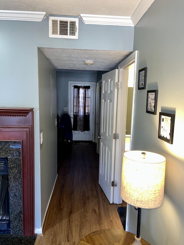 corridor featuring crown molding, visible vents, a textured ceiling, wood finished floors, and baseboards