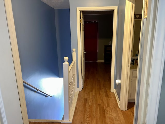 hall with baseboards, wood finished floors, and an upstairs landing