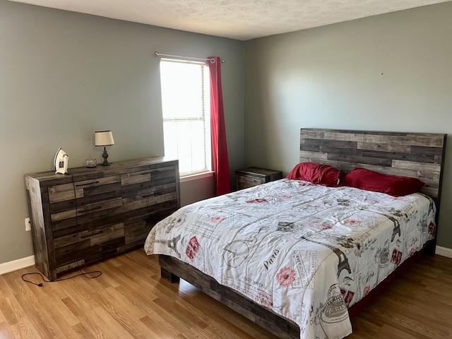 bedroom with a textured ceiling, wood finished floors, and baseboards