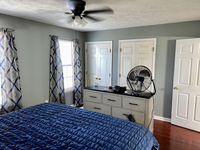 bedroom featuring multiple closets, dark wood-style flooring, a textured ceiling, and baseboards