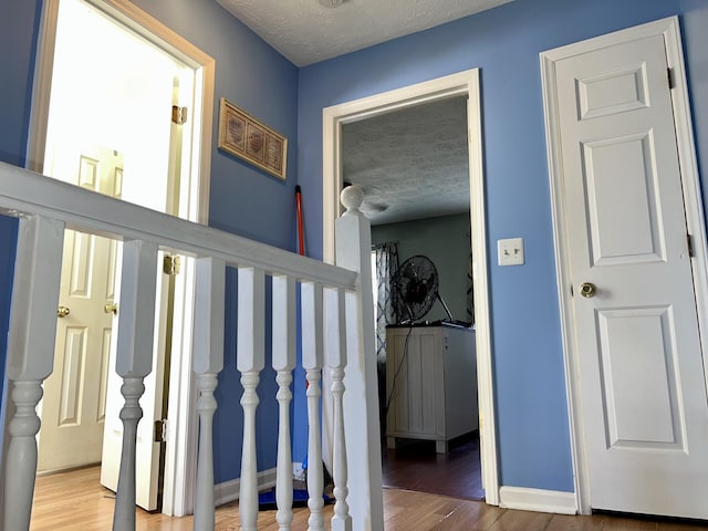 corridor featuring a textured ceiling, baseboards, and wood finished floors