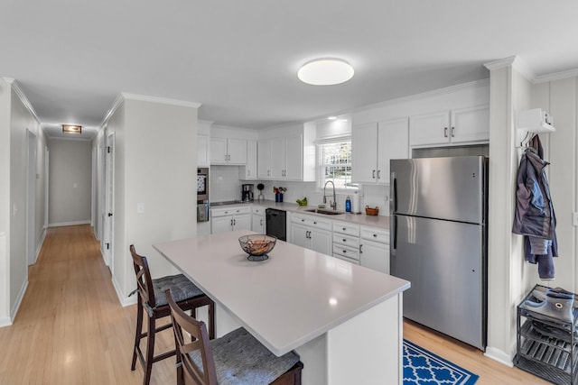 kitchen with a breakfast bar area, appliances with stainless steel finishes, light countertops, white cabinetry, and a sink