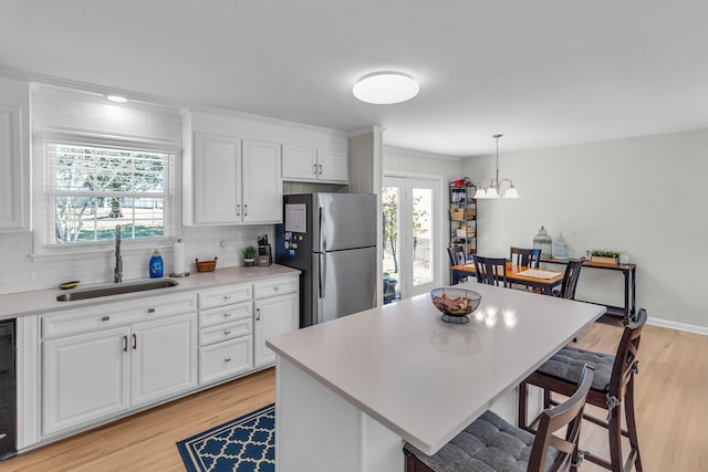 kitchen with light countertops, freestanding refrigerator, white cabinetry, a sink, and a kitchen breakfast bar