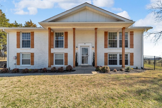 view of front of house featuring brick siding, board and batten siding, a front yard, and fence