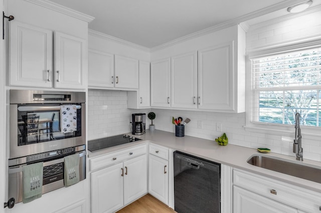 kitchen featuring decorative backsplash, white cabinets, light countertops, black appliances, and a sink