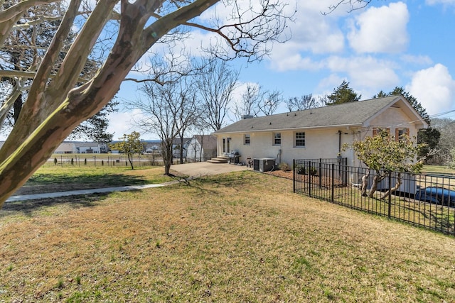 rear view of house with central AC unit, fence, a yard, stucco siding, and a patio area