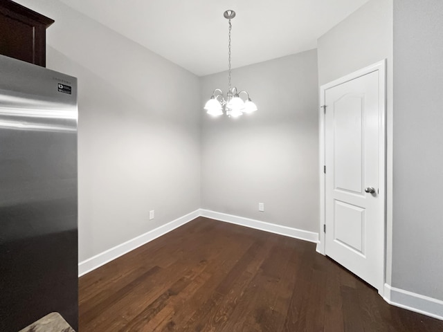 unfurnished dining area featuring dark wood-style floors, baseboards, and an inviting chandelier