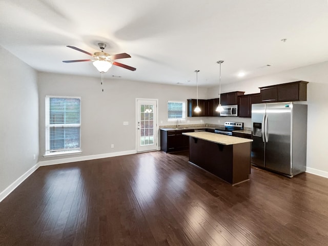 kitchen featuring stainless steel appliances, dark wood-style flooring, dark brown cabinets, light countertops, and a center island