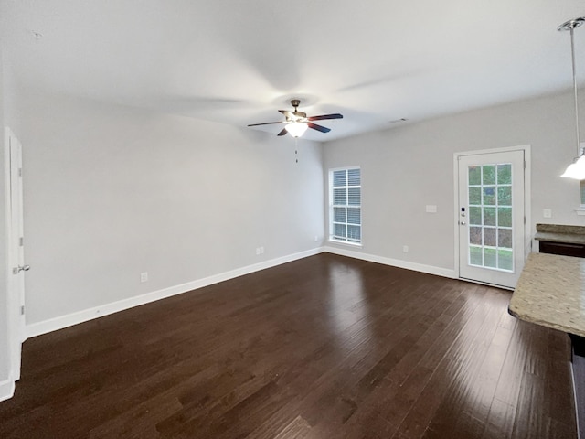 unfurnished living room with dark wood-style flooring, a ceiling fan, and baseboards