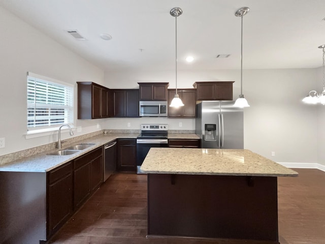 kitchen featuring dark brown cabinetry, dark wood-type flooring, a kitchen island, a sink, and appliances with stainless steel finishes