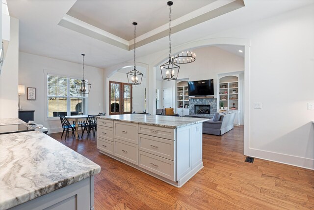 kitchen featuring light wood-type flooring, a tray ceiling, a fireplace, and built in shelves