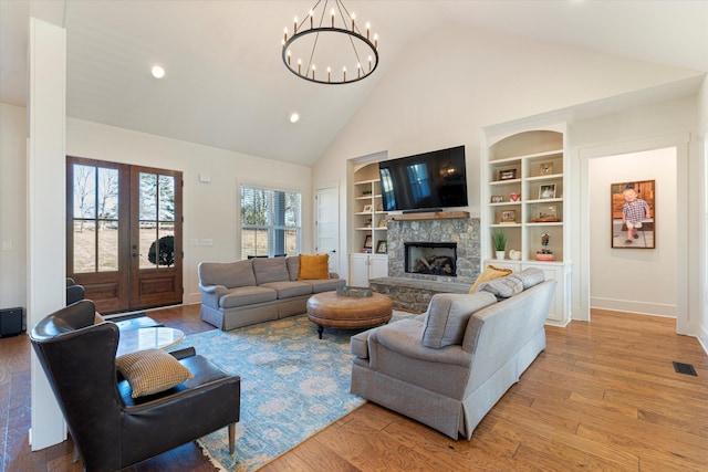 living area with high vaulted ceiling, a stone fireplace, visible vents, built in features, and light wood-type flooring