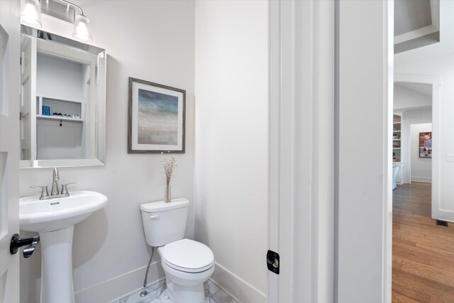 half bathroom featuring a sink, wood finished floors, toilet, and baseboards