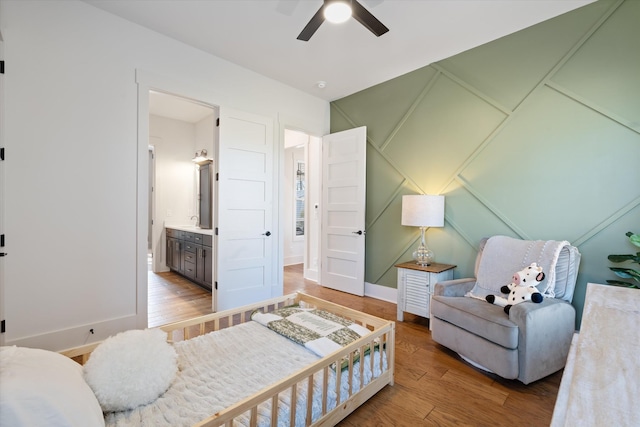 bedroom with ensuite bathroom, light wood finished floors, a sink, and baseboards