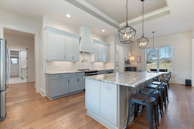 kitchen with light wood finished floors, a tray ceiling, light stone counters, and decorative backsplash