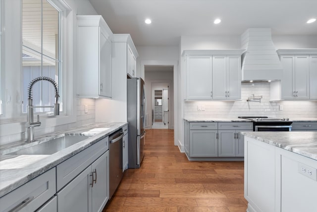 kitchen featuring custom exhaust hood, stainless steel appliances, light wood-style floors, a sink, and recessed lighting