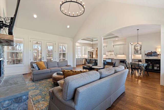 living area with arched walkways, french doors, dark wood finished floors, high vaulted ceiling, and a chandelier