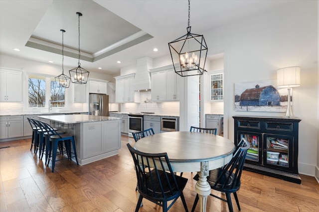 dining area with a tray ceiling, light wood-type flooring, and a notable chandelier