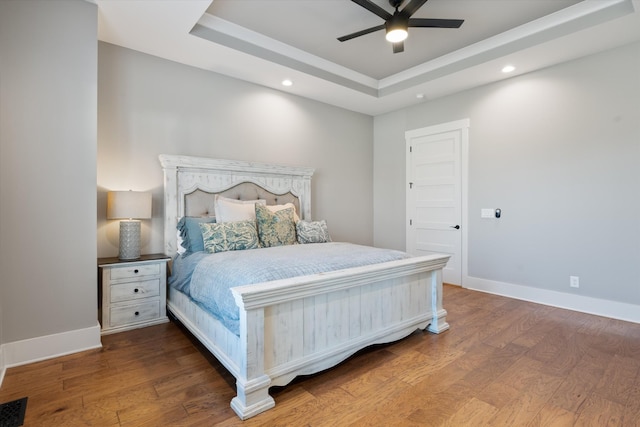 bedroom featuring baseboards, a tray ceiling, and wood finished floors