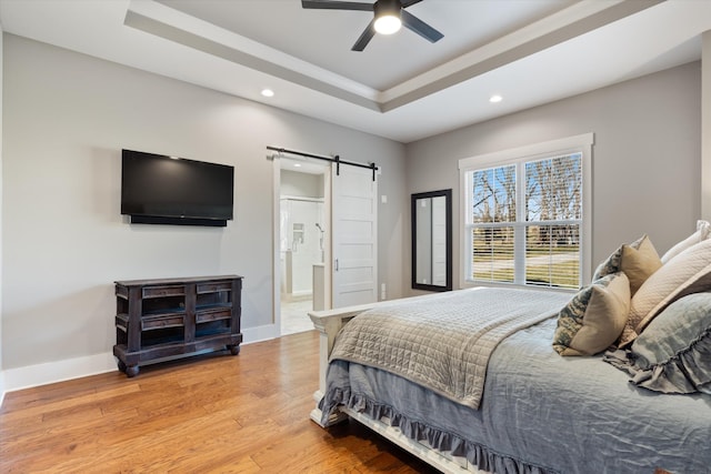 bedroom with a raised ceiling, a barn door, light wood-style floors, connected bathroom, and baseboards