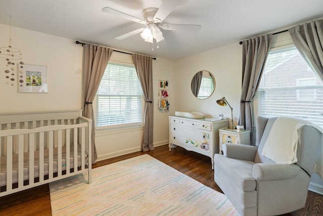 bedroom with a crib, baseboards, a ceiling fan, and wood finished floors