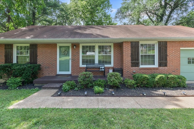 ranch-style home featuring a shingled roof, covered porch, brick siding, and an attached garage