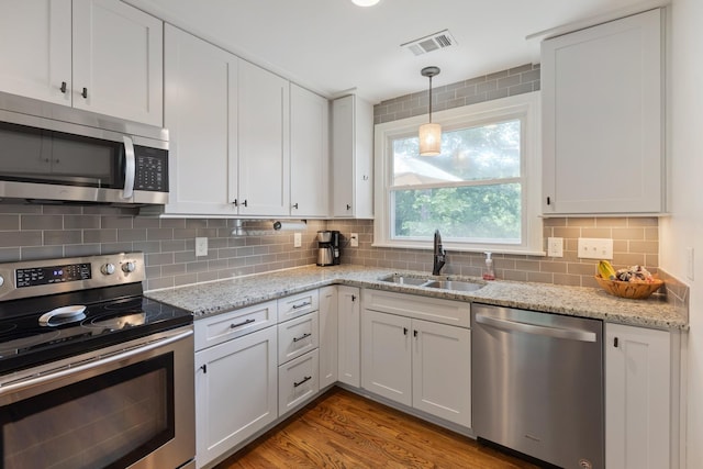 kitchen with stainless steel appliances, a sink, visible vents, light wood-type flooring, and decorative backsplash